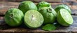   A pile of limes sits atop a wooden table, adjacent to a leafy green fruit