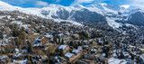 Fototapeta Miasto - Aerial panoramic view of the Verbier ski resort town in Switzerland. Classic wooden chalet houses standing in front of the mountains. 