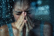 A woman is wiping her nose with a tissue while looking out the window at rain