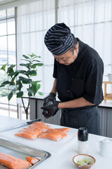Wall Mural - Asian chef putting salt and Black pepper on salmon. Man cutting raw salmon and Sprinkle with black pepper.