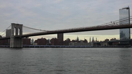 Wall Mural - water flowing under the brooklyn bridge (east river new york city harbor downtown) landmark tourist destination suspension bridge at sunset footage (nyc travel)