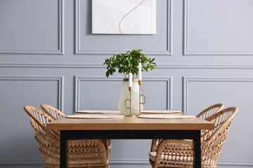 Wall Mural - Rattan chairs, table, burning candles and vase with green branches in stylish dining room