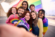© CarlosBarquero - Group of young diverse friends taking a selfie looking at front camera of mobile celebrating gay pride day together holding rainbow flag. LGBT people community smiling and having fun outdoor