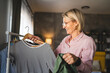 One mature blonde woman at home choose and sort clothes on hanger