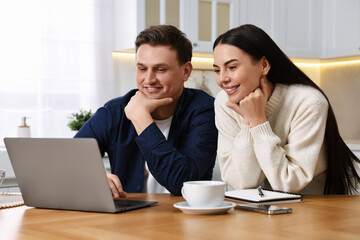 Canvas Print - Happy couple using laptop together at wooden table in kitchen