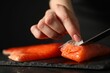 Chef removing scales from salmon for sushi at dark table, closeup
