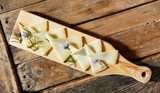 Fototapeta Londyn - From above of delicious cheese slices served with rosemary sprouts and flowers on wooden cutting board in restaurant