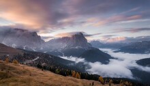 mountains in fog at beautiful sunset in autumn in dolomites italy landscape with alpine mountain valley low clouds trees on hills purple sky with clouds at dusk aerial view passo giau nature