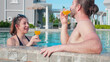 Happiness couple relax in swimming pool together at hotel resort, summer and honeymoon, boyfriend and girlfriend in weekend with relax while drinking juice orange, relation and leisure in summertime.