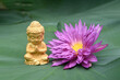 Close-up of Buddha Statue with beautiful blooming lotus flower on green leaf