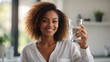 A beautiful young African American black woman in white shirt is holding, drinking a glass cup of water in the morning, blurred white modern home background, healthy lifestyle concept