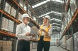 © SKW - A man and a woman are standing in a warehouse, looking at a laptop. The man is wearing a hard hat and the woman is wearing a yellow vest. They seem to be discussing something important