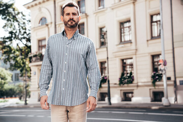 Wall Mural - Portrait of handsome confident stylish hipster lambersexual model. Sexy modern man dressed in blue shirt and trousers. Fashion male posing on street background in Europe city at sunset, sunglasses