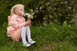 © somemeans - Little girl in pink dress in the garden. Girl sitting with blooming branch and snuffles their. Spring day