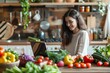© Anastasiia - Young Woman Sits With A Laptop At A Table In The Kitchen Surrounded By Greens And Vegetables. Concept Macrobiotic Diet
