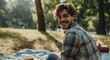 young handsome man or student sitting in the park on a picnic blanket in a good mood in nature