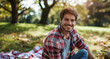 young handsome man or student sitting in the park on a picnic blanket in a good mood in nature
