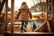 Boy in jacket plays on playground, view from the back. Abstract image of preschool child playing outdoors