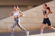Two young women in sportswear are running on modern buildings background. Active lifestyle concept