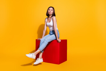 Sticker - Full length photo of flirty sweet woman wear white singlet sitting red cube sending kiss isolated yellow color background