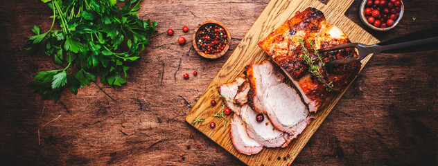 Baked festive pork butt or ham with herbs, spices and cranberries for sauce, served and sliced on cutting board, rustic wooden table background, top view