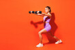 Full body young fitness instructor woman sportsman wear top shorts purple clothes train in home gym hold dumbbells do squats lunges isolated on plain orange background. Workout sport fit abs concept.