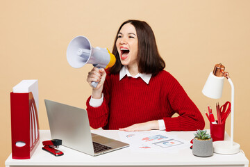 Wall Mural - Young employee business woman wear red sweater shirt sit work at office desk with pc laptop hold megaphone scream announces sale Hurry up isolated on plain beige background Achievement career concept