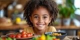 Fototapeta Sport - A cheerful black toddler girl enjoys a plate of macaroni and cheese with tomatoes.