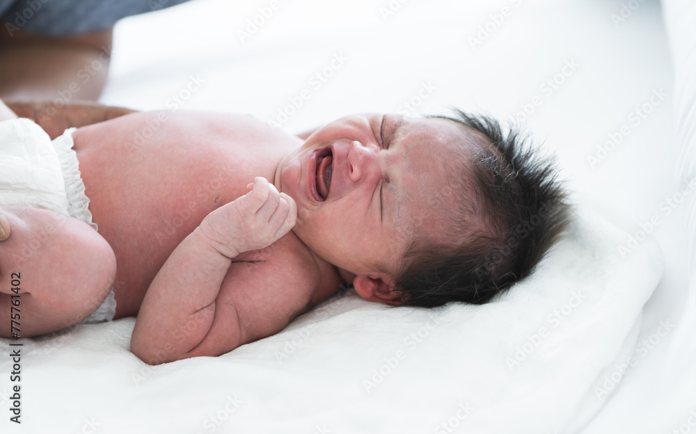 Newborn baby girl crying and screaming, lying on bed at home. Asian Australian infant 19 days old wear diaper, showing unhappy emotion face expression