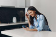 © SHOTPRIME STUDIO - Young woman sitting at table with cell phone, scrolling through content and looking at screen attentively