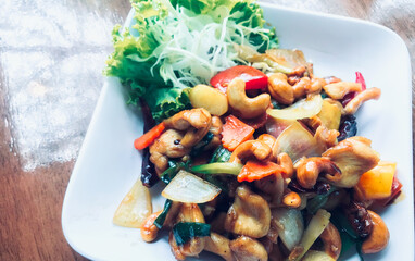 Wall Mural - Thai food, stir-fried chicken with cashew nuts on a white plate, food plate on a wooden table with natural light from the window.