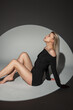 © alones - Beautiful sensual blonde woman with a slim body and legs in a black sexy dress sits and poses on a dark background in the studio