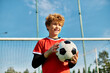 © LIGHTFIELD STUDIOS - A young boy stands in front of a soccer goal, holding a soccer ball with a determined expression. He is positioned for a kick, showcasing his love for the sport and his readiness to score a goal.