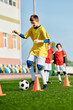 © LIGHTFIELD STUDIOS - A lively group of young boys kicking a soccer ball around cones on a vibrant field, showcasing teamwork and skill in action.