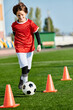 © LIGHTFIELD STUDIOS - A young boy demonstrating his soccer skills by kicking a soccer ball around orange cones on a field. His precise footwork and agility are evident as he navigates through the obstacles with ease.