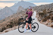 © KatyaPulka - Woman cyclist enjoying beautiful seaside view during sunset amidst her training, with mountains in the background. Woman cyclist wearing cycling kit and helmet. Calp, Alicante, Spain.