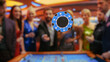 Casino Players Making Bets at a Roulette Table. A crowd of International People Enjoying Nightlife in City. Male Gambler Tossing a Casino Chip with a Template Placeholder Flying At the Camera.