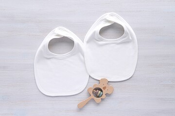 Canvas Print - Two white cotton baby bibs, mockup for design presentation, simple minimal composition on white wood background with wooden baby rattle.