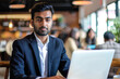 Portrait of young Indian businessman using laptop in a coffee shop.
