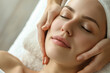 © Welle Photos - Young woman getting a facial treatment in a beauty salon, in a closeup of hands applying cream on her face with her eyes closed and a towel over her head