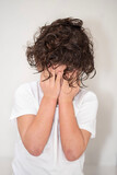 Fototapeta  - A young boy with curly black hair covering his face with his hands