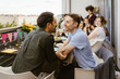 © Maskot - Romantic gay couple looking at each other while sitting with friends at dinner party in balcony