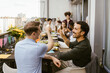 © Maskot - Happy men toasting drinks with group of friends sitting at dining table in balcony