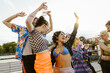 © Maskot - Carefree multiracial non-binary friends dancing with each other in city