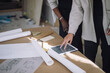 © Maskot - Midsection of female constructor engineer explaining blueprint to colleague over digital tablet on table at under constr
