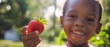 The boy holds out a strawberry in the frame, close-up