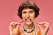 © LIGHTFIELD STUDIOS - funny pierced girl in 20s biting two different flavors of sweet and sour candies on pink backdrop