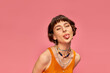 © LIGHTFIELD STUDIOS - cheeky carefree girl in 20s with short brunette hair sticking tongue out on pink background