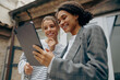 © Daria - Smiling female business people standing at office terrace and using digital tablet together