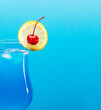 Close up of blue lagoon cocktail garnished with a slice of lemon and cherry isolated on turquoise background with space for text.